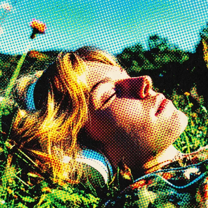 Woman listening to headphones outdoors, reclining with her eyes closed in the sun.